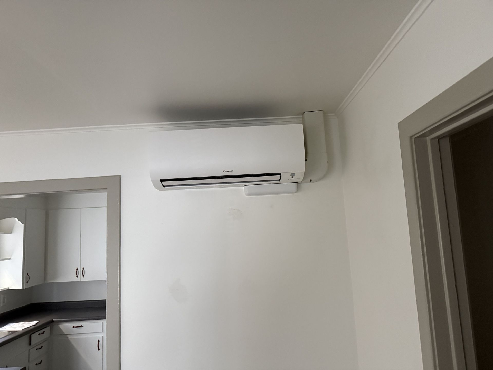 White air conditioning unit mounted on a white wall in a room, near a doorway.