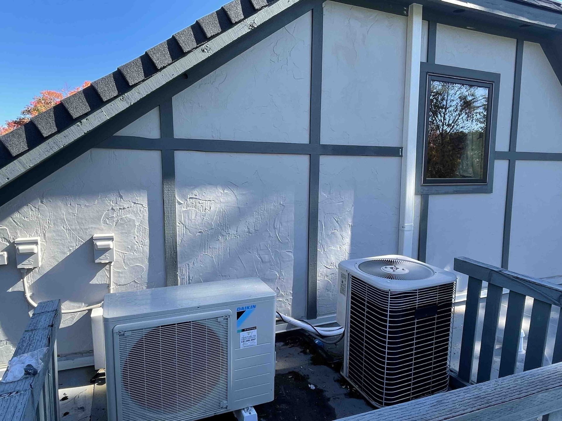 An air conditioning unit and rooftop components on a white wall with dark gray trim.