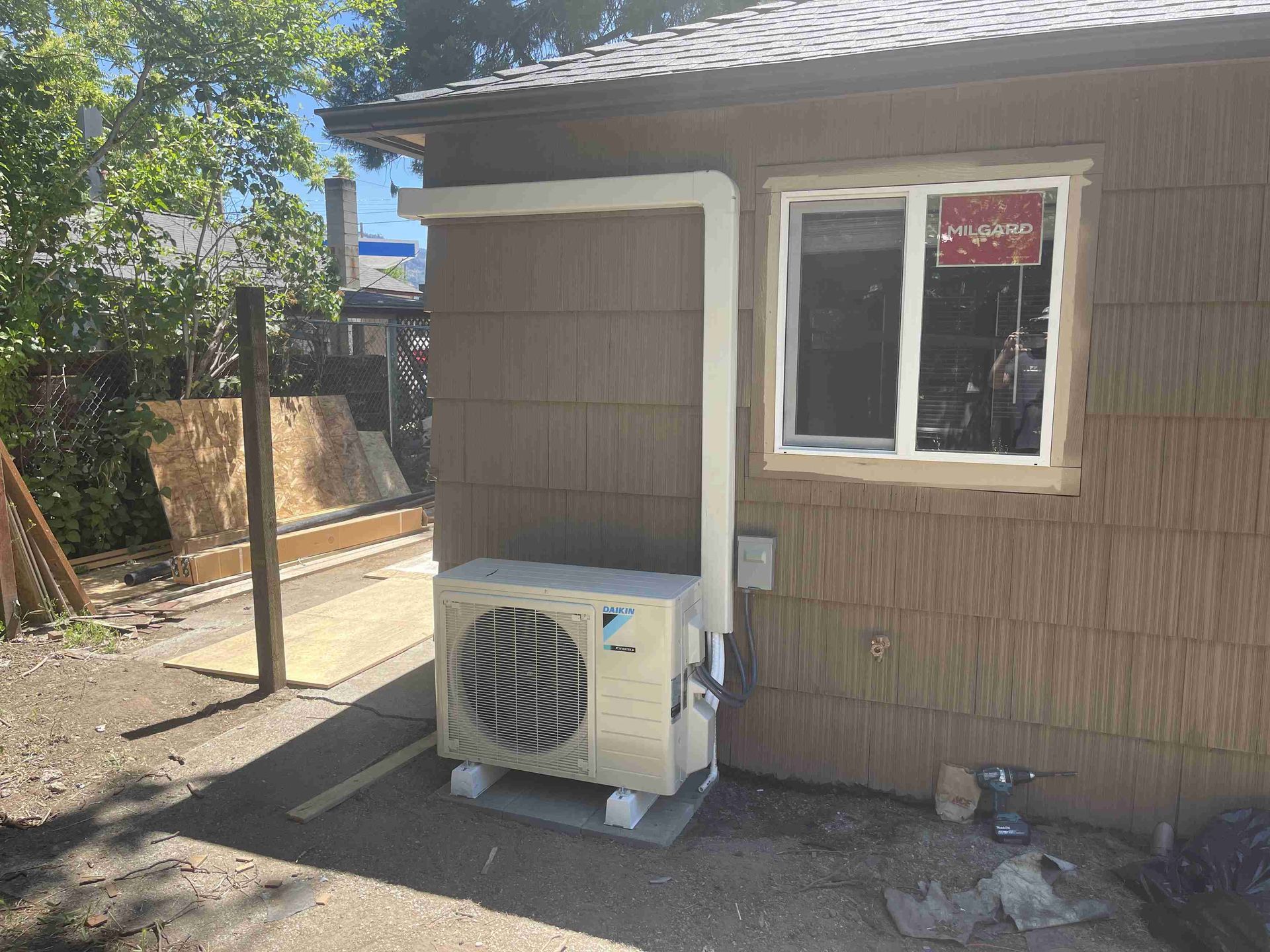 Outdoor HVAC unit mounted on concrete blocks beside a building with brown siding and a window.
