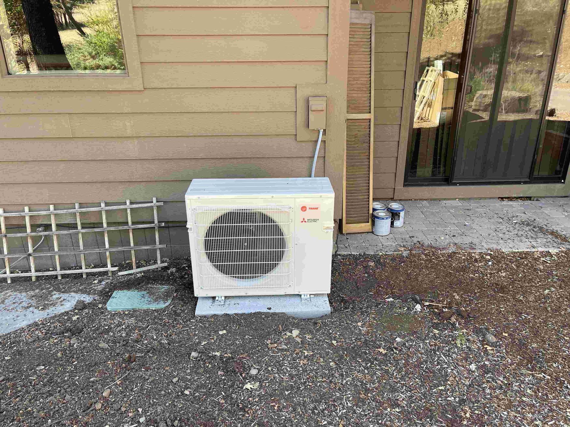 Exterior air conditioning unit on a gravel surface next to a building with a window and a sliding glass door.