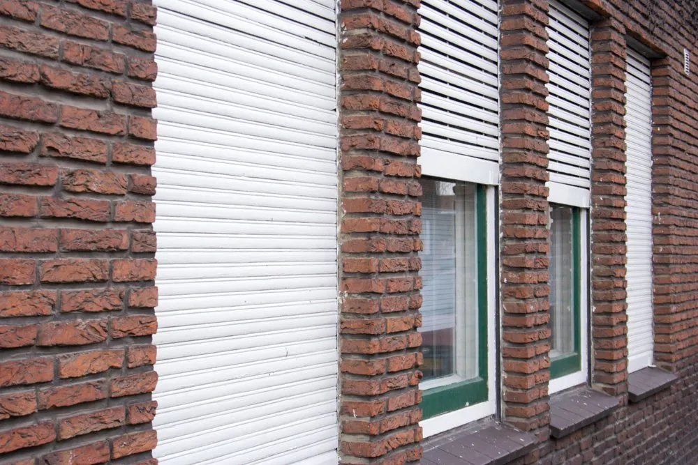 A Brick Building with White Roller Shutters on The Windows — Manning Valley Patios in Taree, NSW
