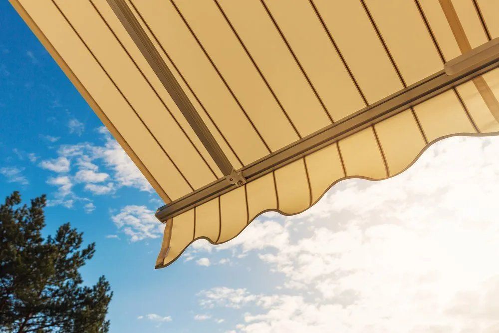 A Beige Awning Is Against a Blue Sky with Clouds — Manning Valley Patios in Cundletown, NSW