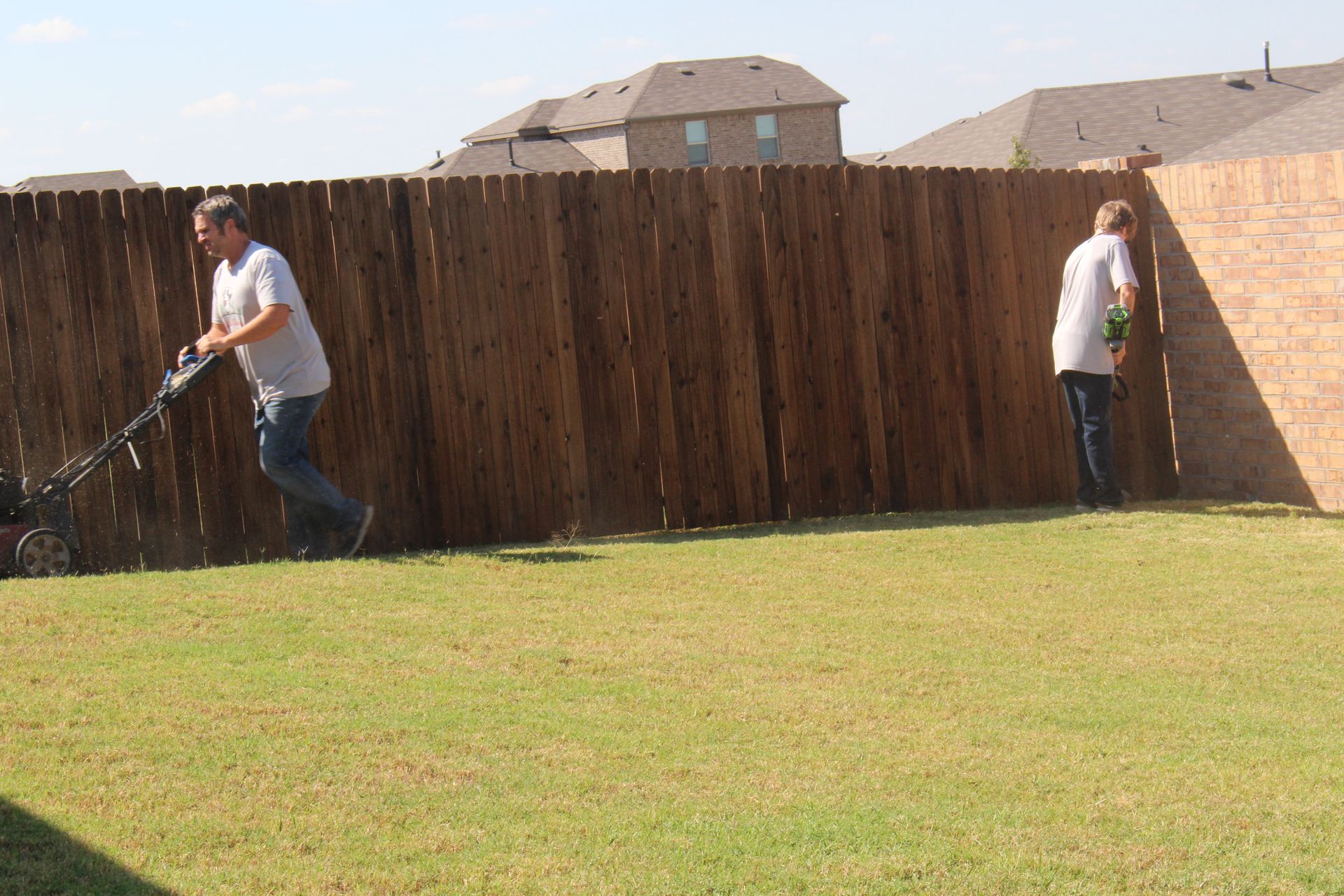 A young man and man mowing the backyard.