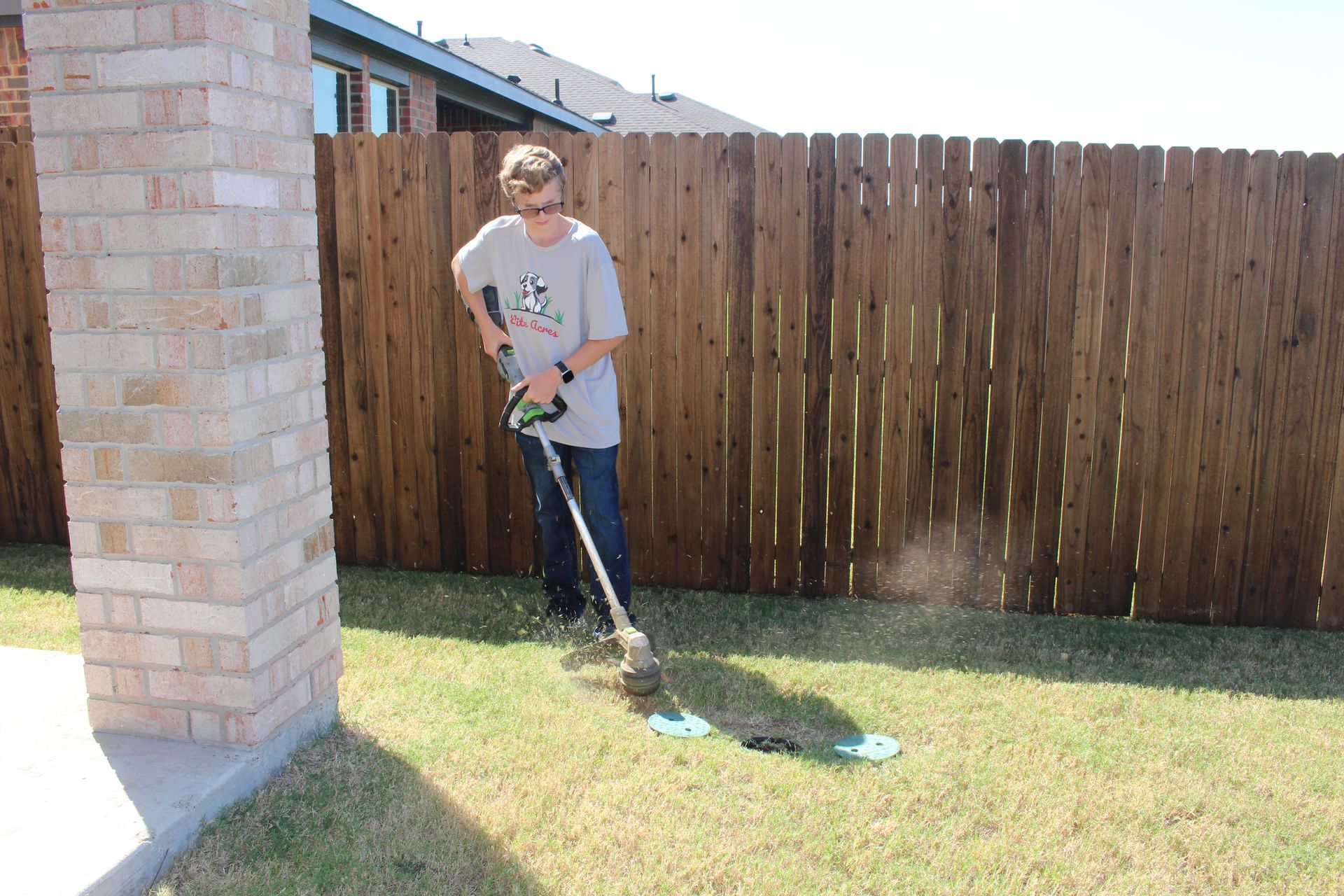 A young man using the grass cutter near the fence.