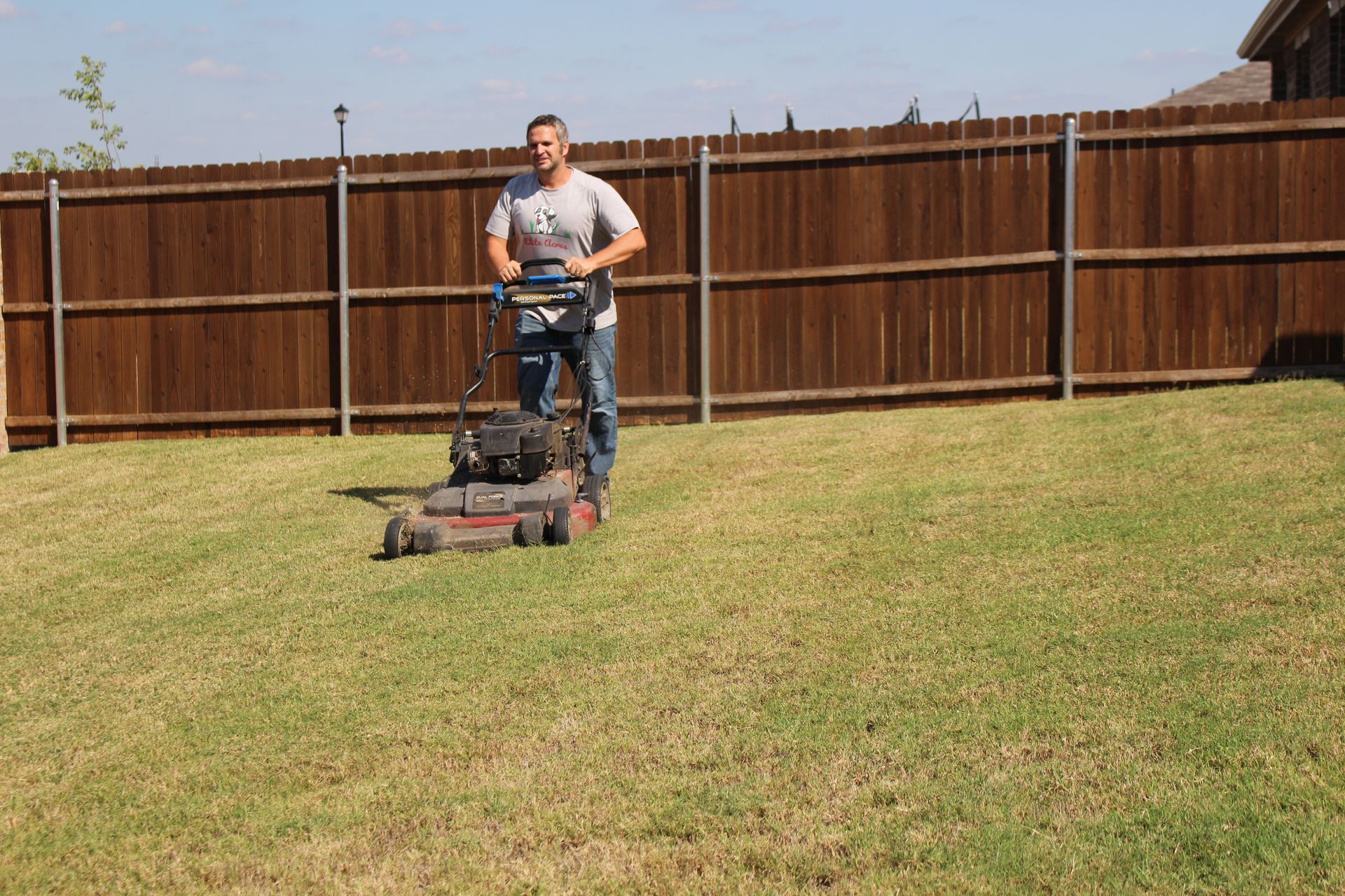 A man is using a lawn mower to cut the grass in his backyard.