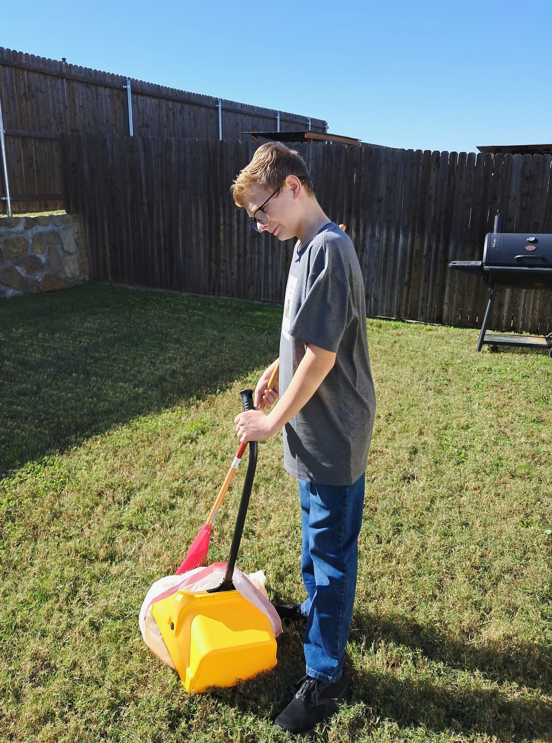 A young boy is standing in the grass holding a yellow bucket.