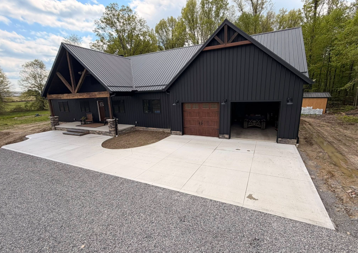 Modern black house with a two-car garage and gravel driveway under a cloudy sky
