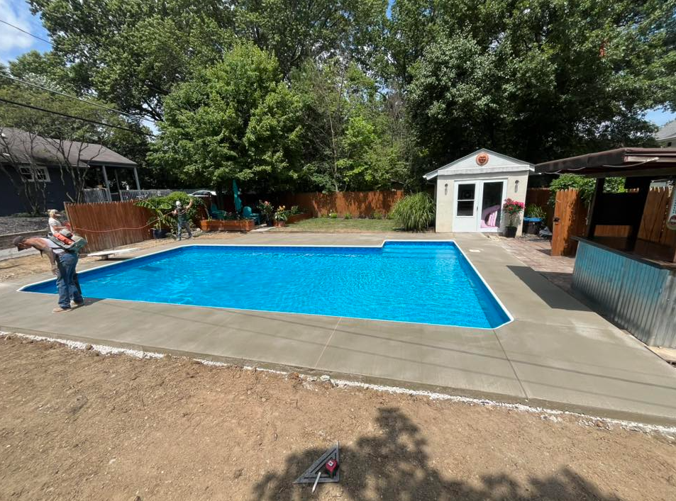 Backyard swimming pool with a person standing at the left and a small white pool house nearby