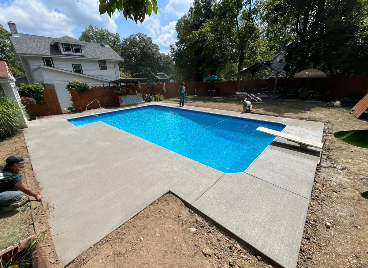 Backyard swimming pool with bright blue water, concrete deck, and a house in the background