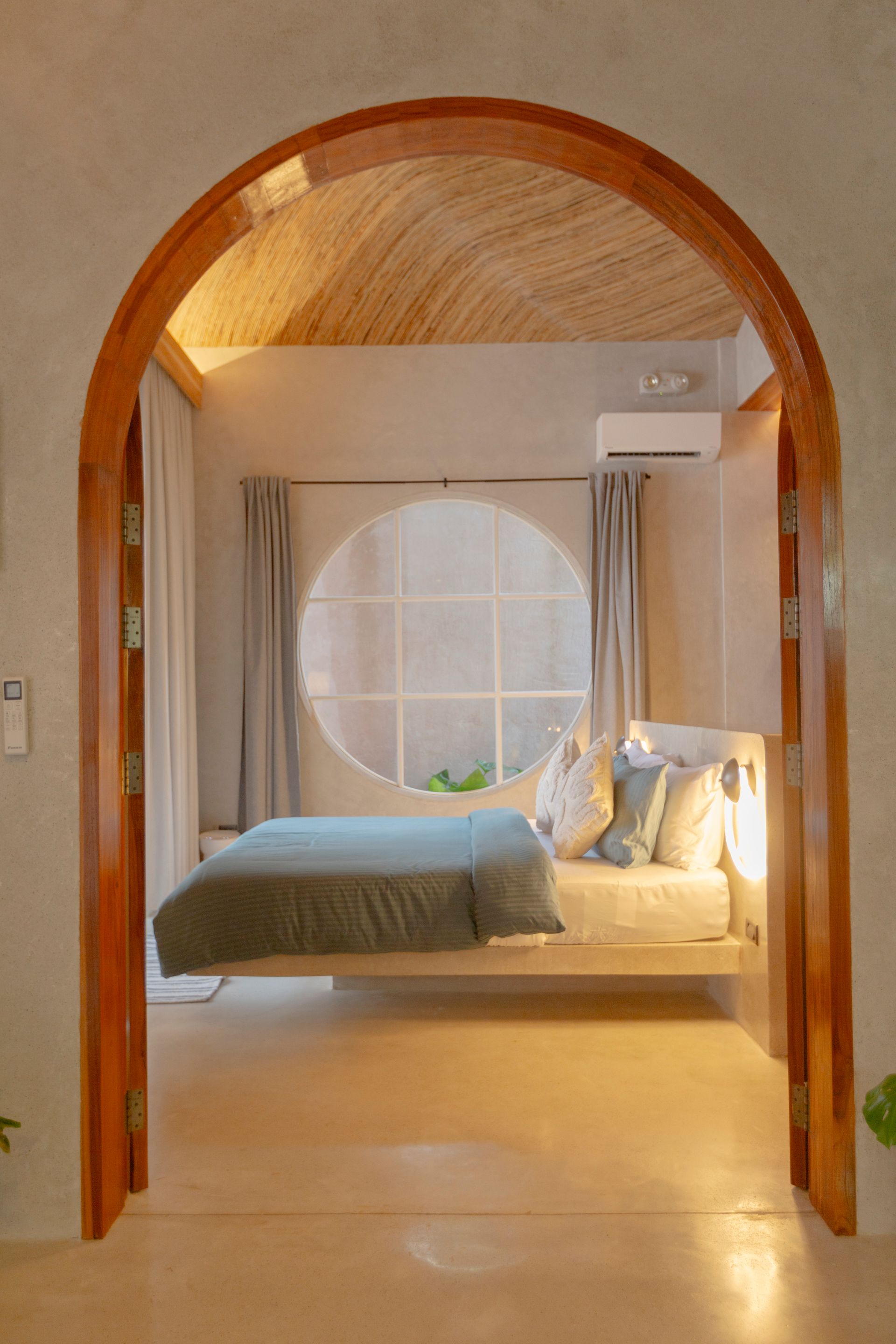 Bedroom with arched doorway, round window, bed with blue blanket, neutral colors.
