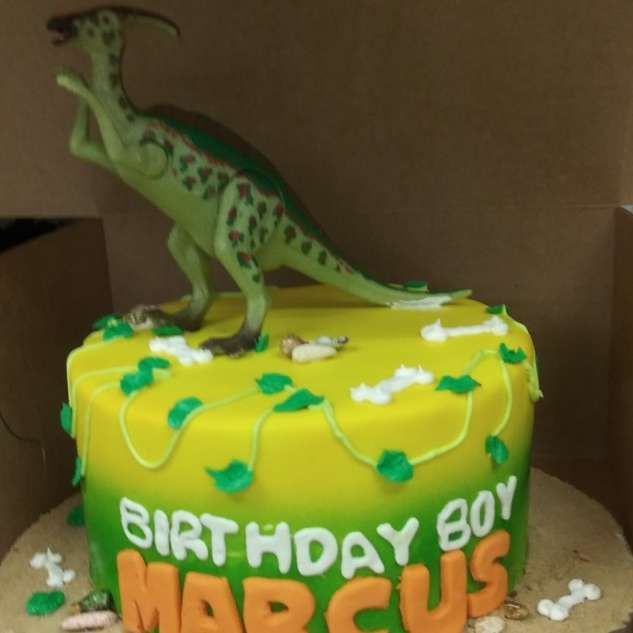 Dinosaur birthday cake with green T. rex topper and “BIRTHDAY BOY” text on yellow frosting