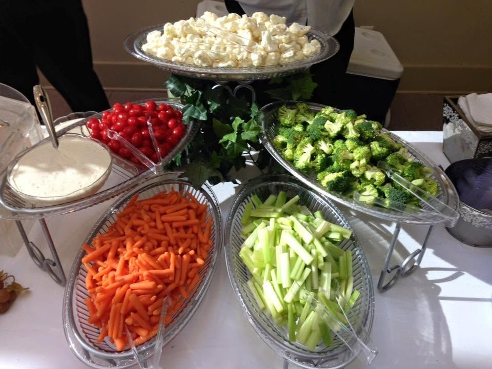 Assorted vegetable and dip trays arranged on a buffet table, including carrots, celery, broccoli, cherries, and cauliflower.