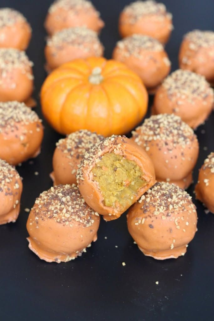 Orange cake pops with sesame-coated tops arranged around a small orange pumpkin on a dark surface