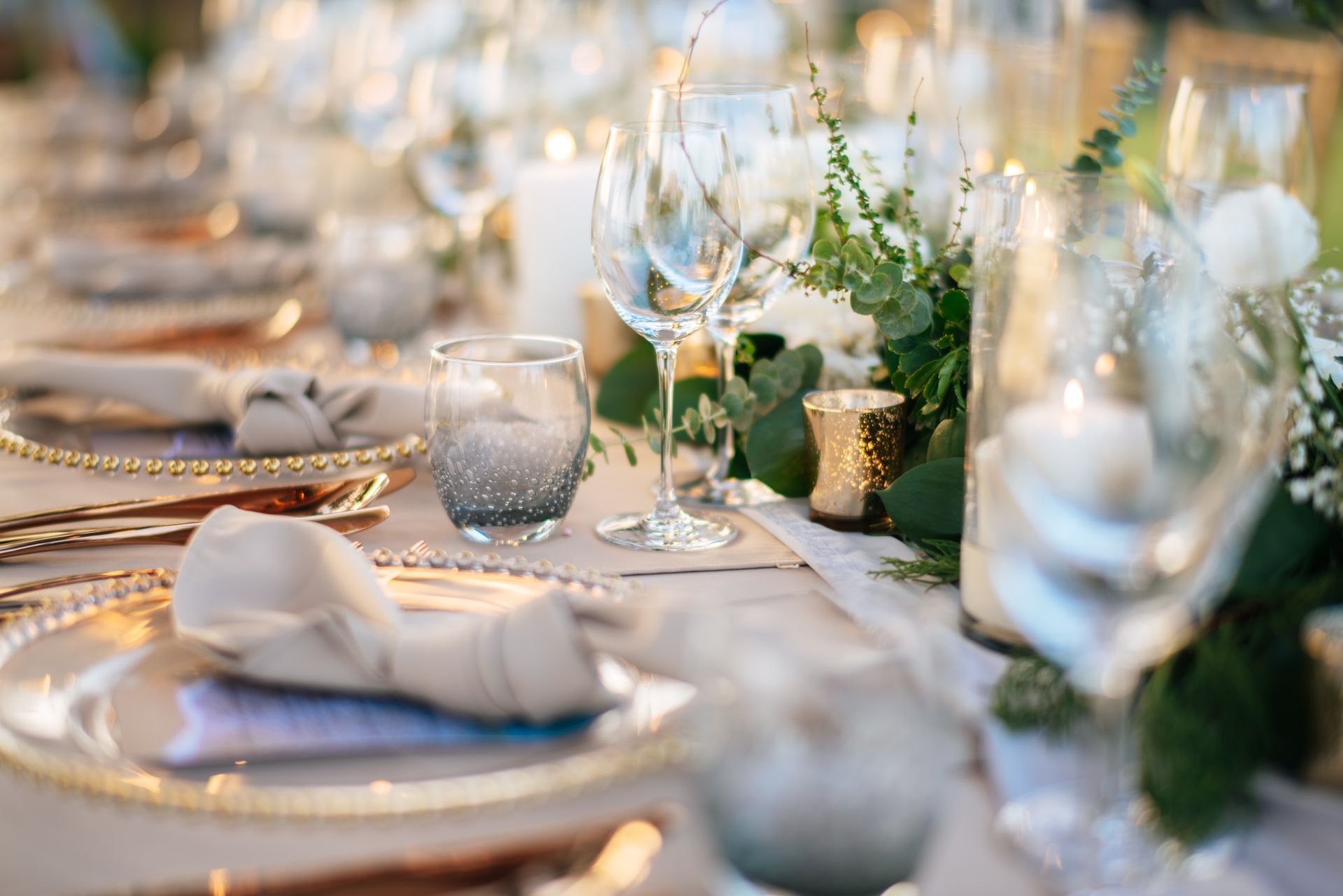 Elegant banquet table set with white linens, gold-rimmed plates, glassware, and white floral centerpieces