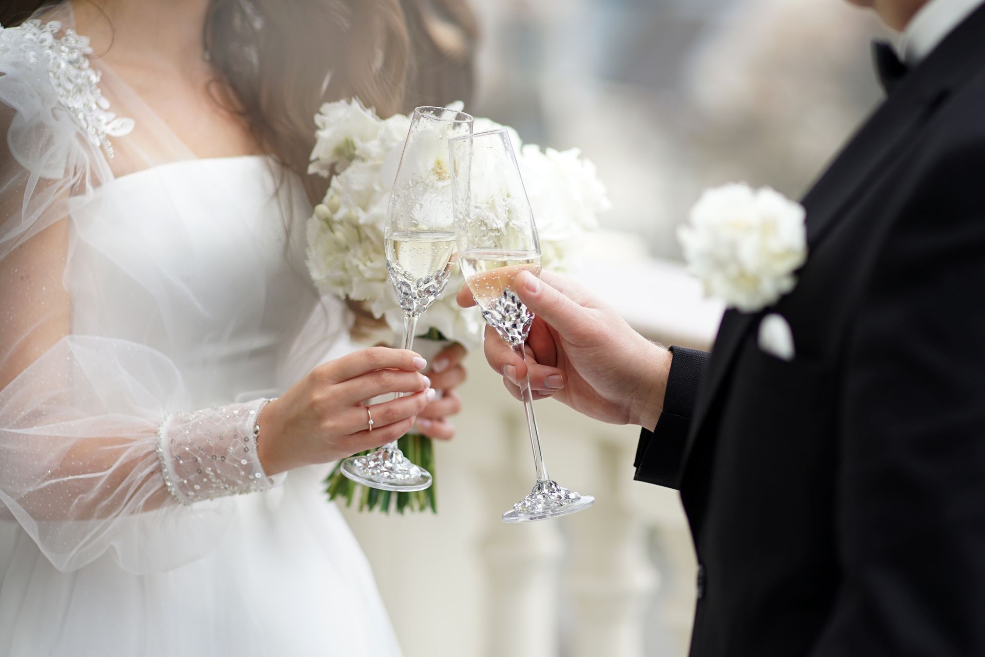 Bride and groom clink champagne glasses beside a white wedding bouquet