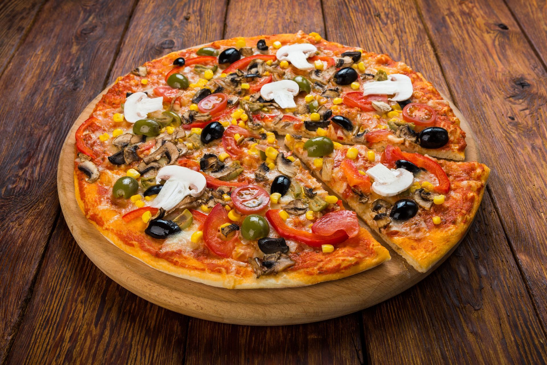 Pizza topped with mushrooms, olives, peppers, and cheese on a wooden board