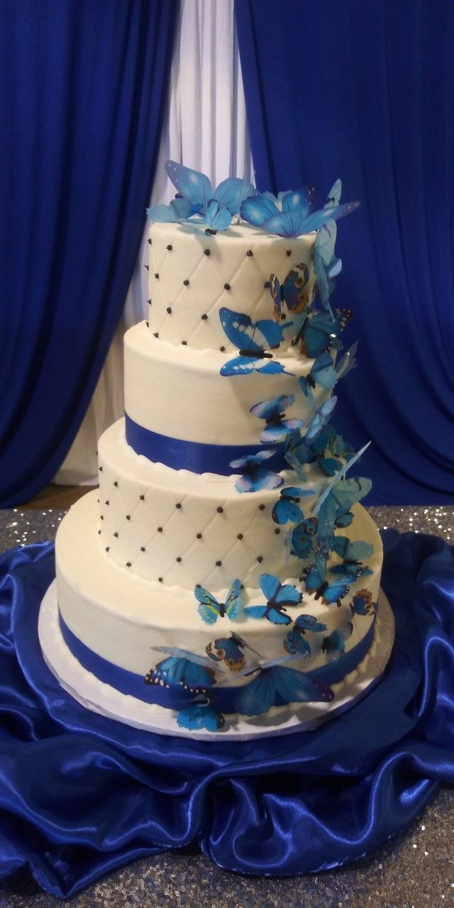 Three-tier white wedding cake with blue ribbon and floral accents on blue satin drapery backdrop