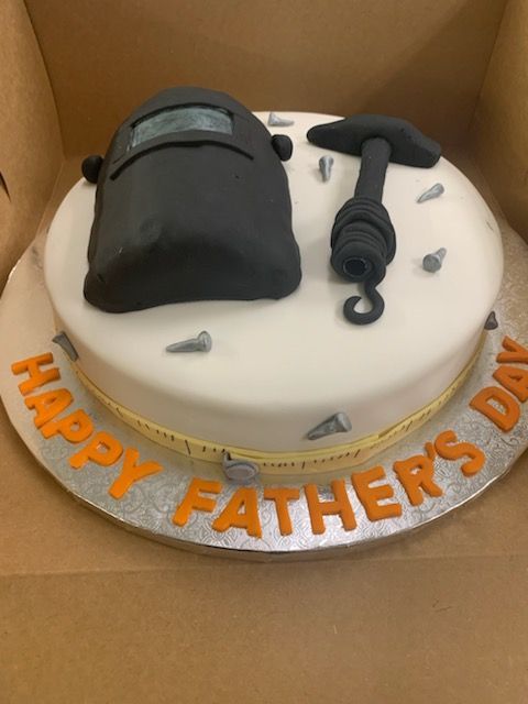Black back massager cake on a white round cake with orange “HAPPY FATHER’S DAY” lettering.