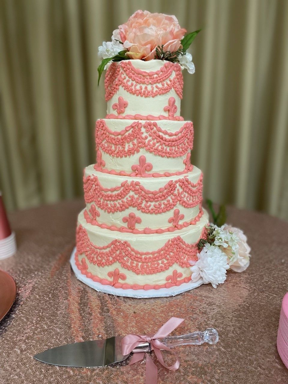 Four-tier white cake with pink lace icing and flowers on a pink tablecloth