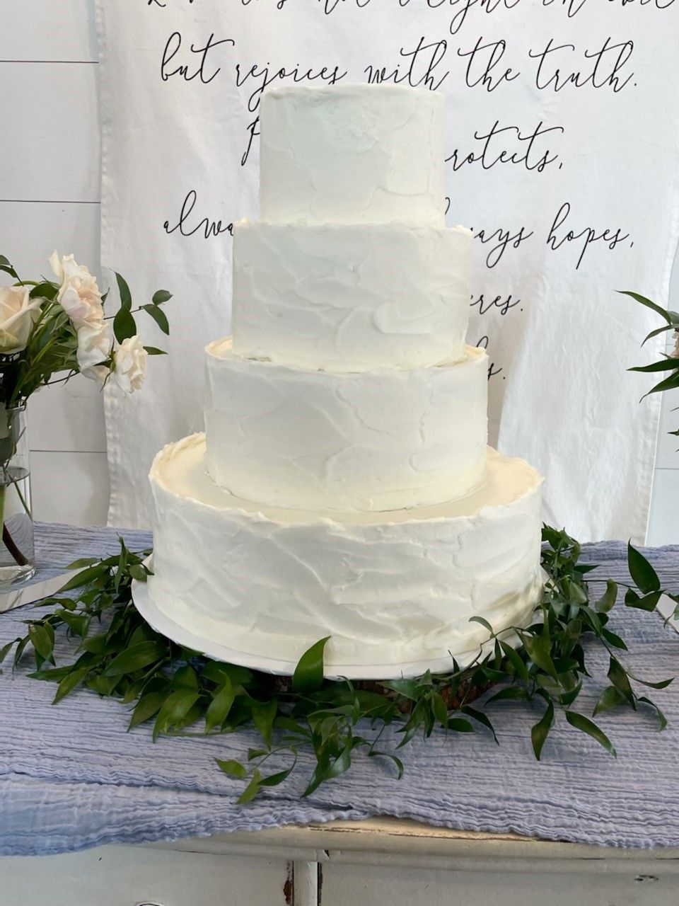 Three-tier white wedding cake on a rustic table with greenery and floral accents