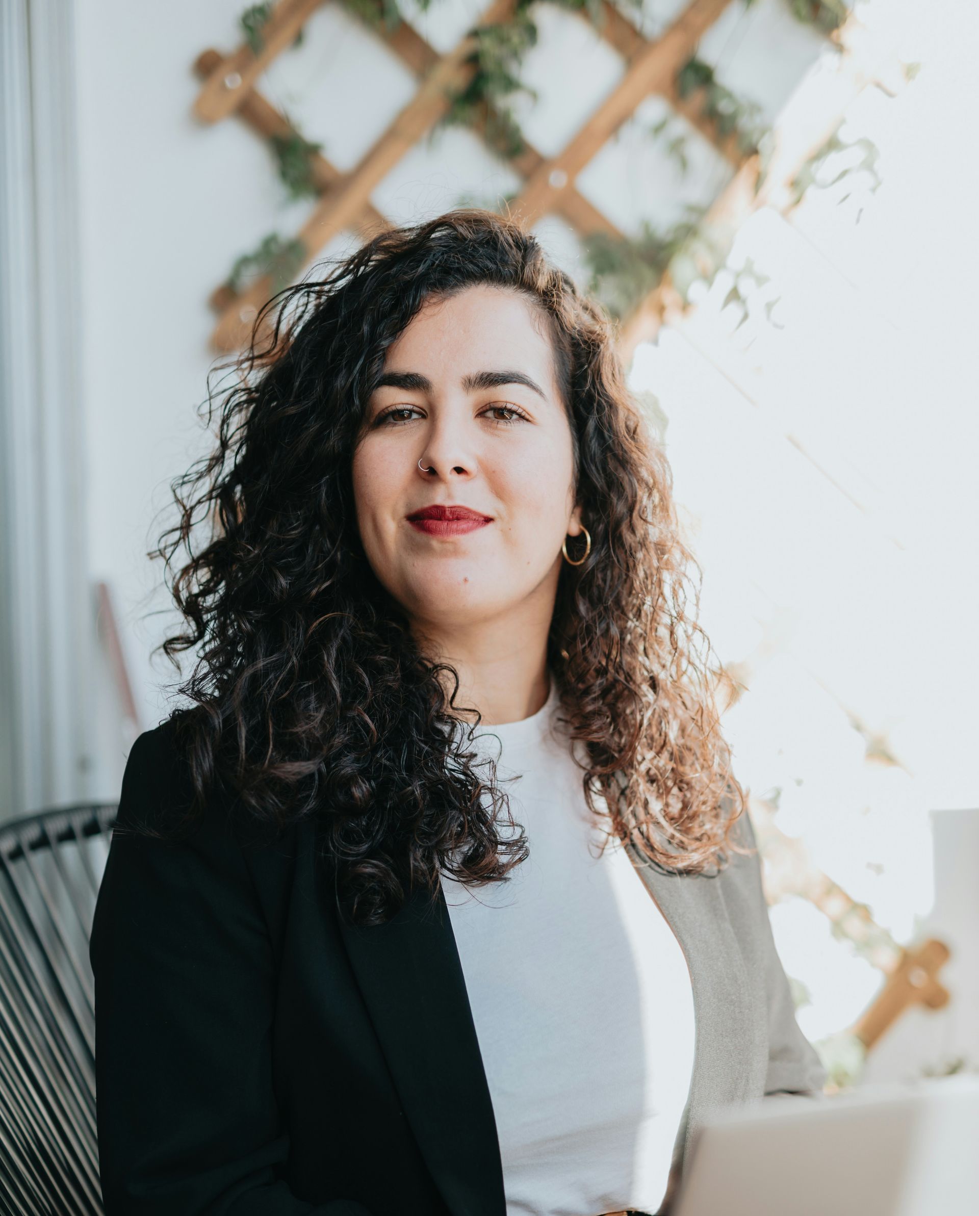 A woman with curly hair is sitting in a chair with a laptop.