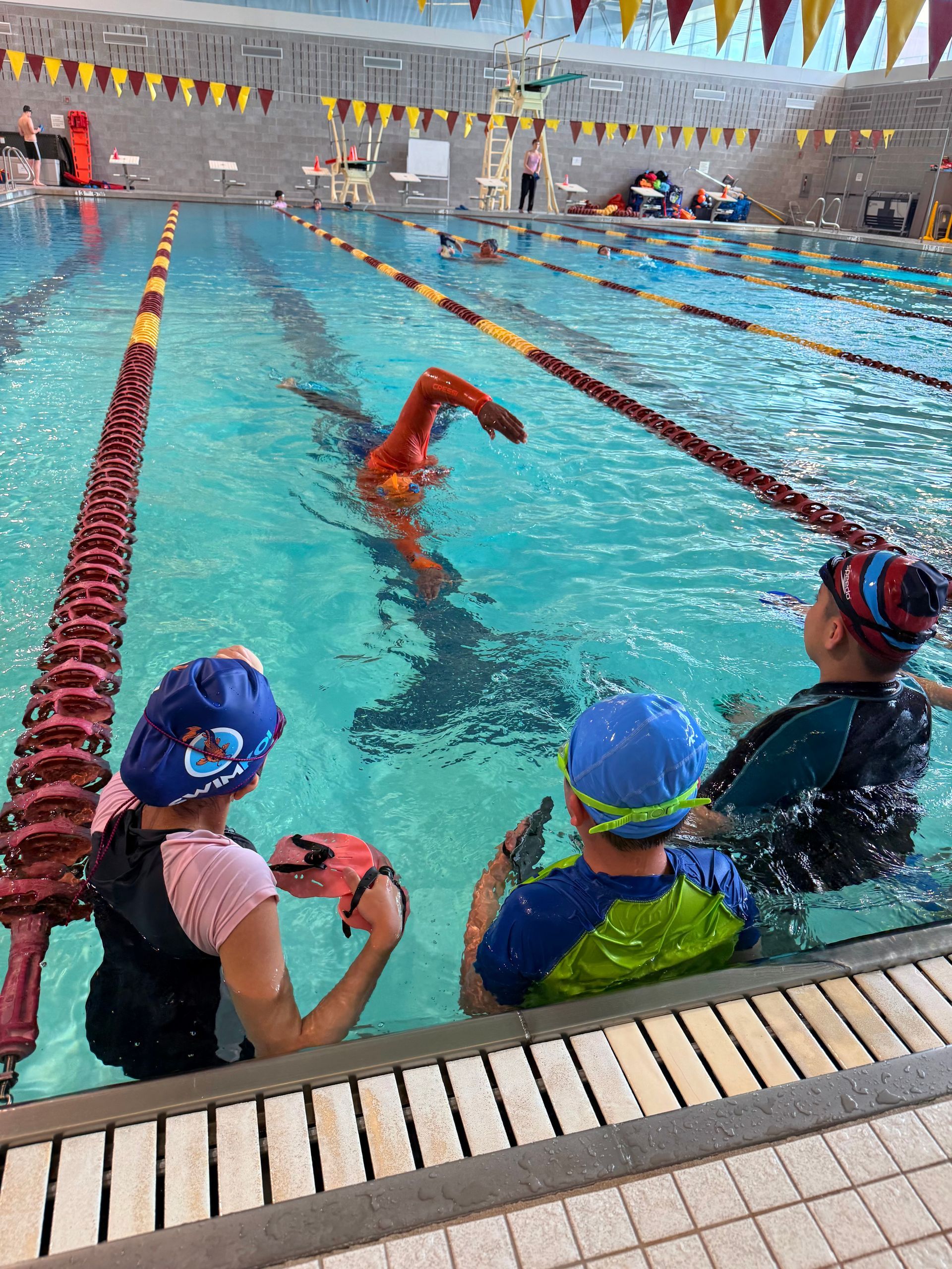 A person guides a child in a pool, teaching them to swim with a kickboard.