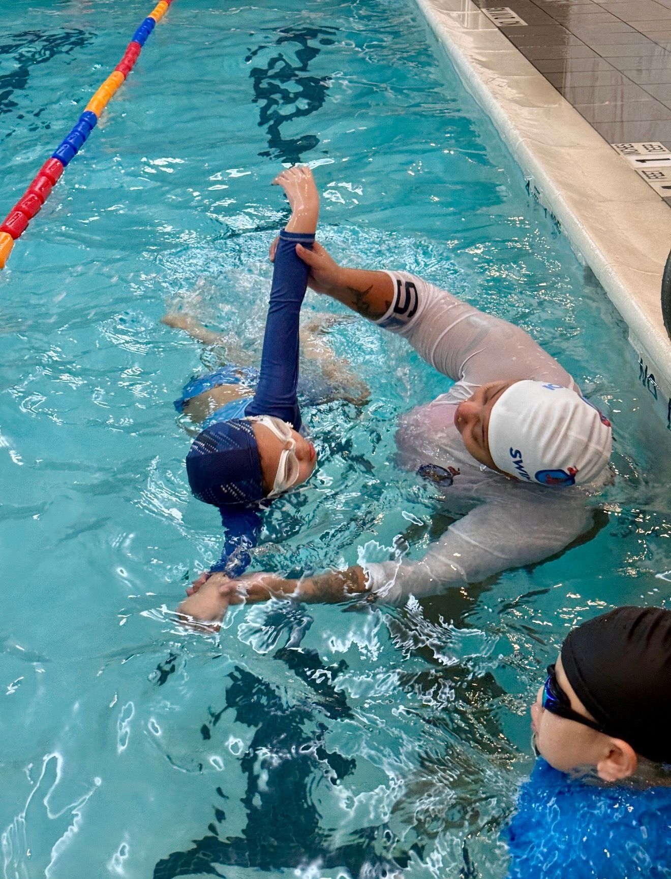 Boy with swim goggles in a pool, smiling and giving thumbs up.