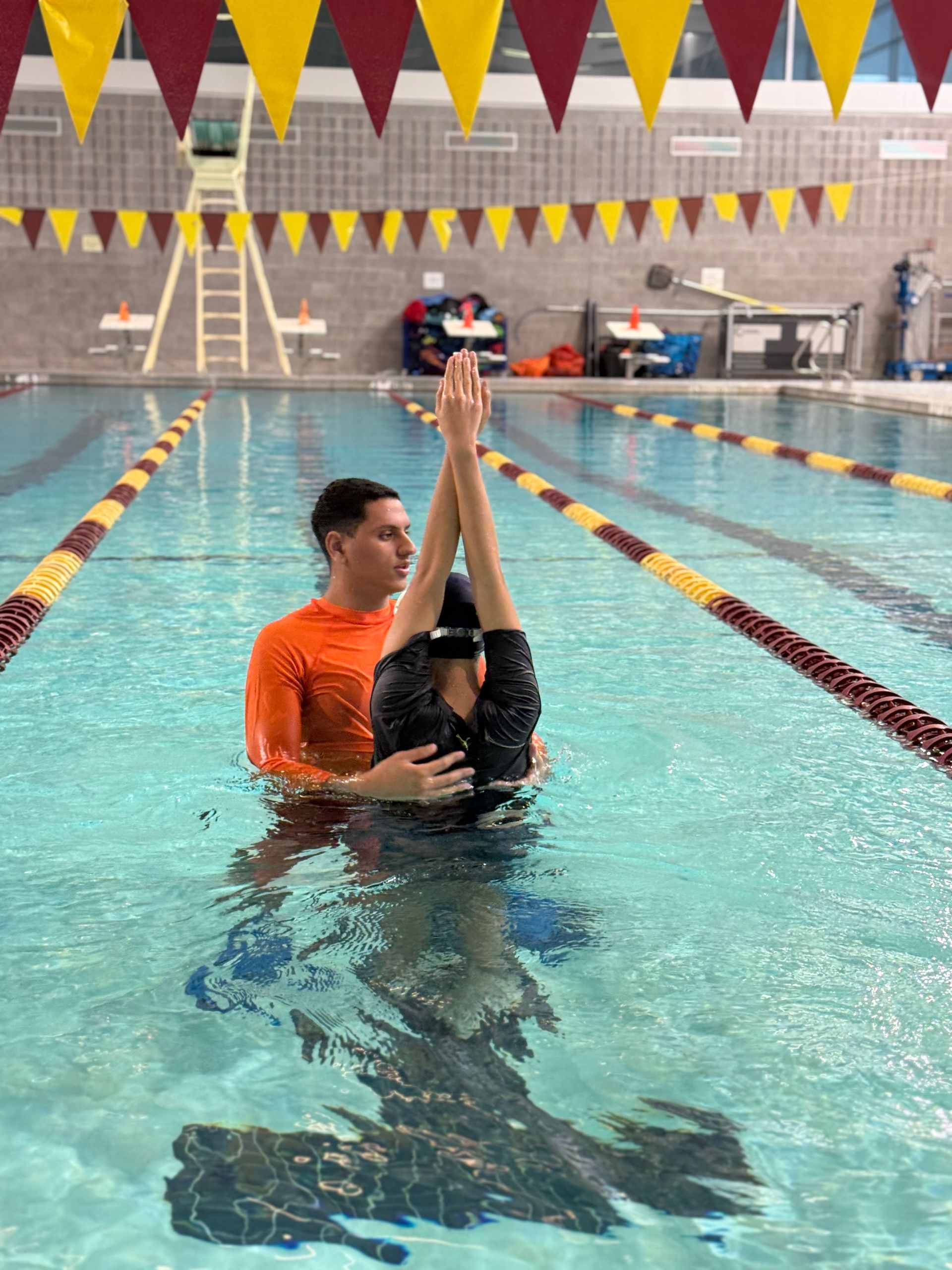 Person in orange shirt swimming breaststroke in a pool, hands creating splashing water.
