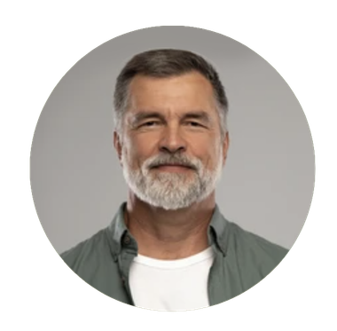 Man with gray beard, smiling, wearing a green shirt over a white t-shirt, against a gray background.