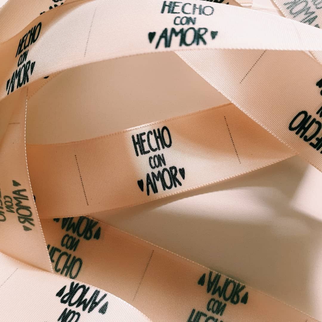 Primer plano de una cinta color melocotón con texto negro que dice “Hecho con amor” sobre un fondo blanco.
