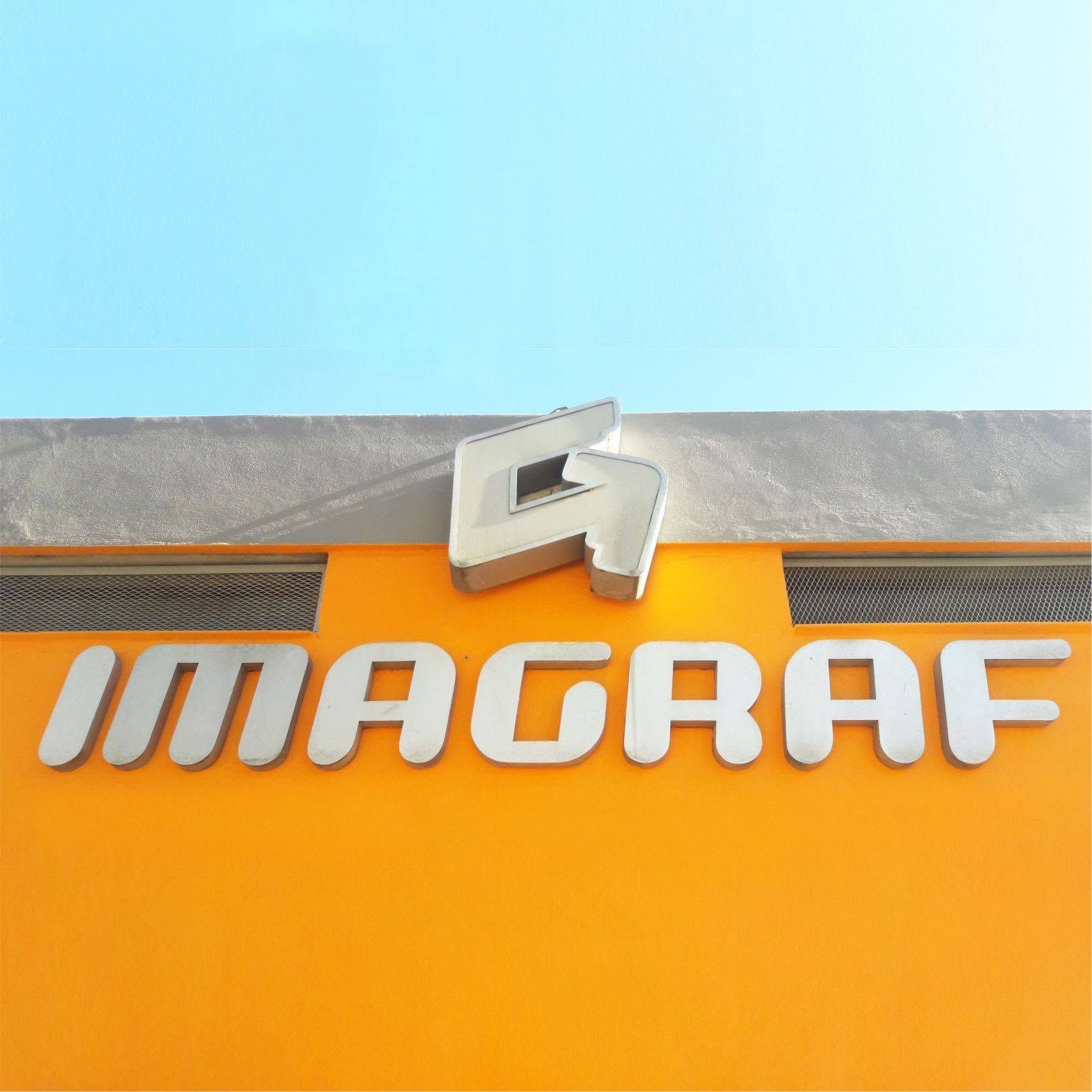 Letrero de MAGRAF con letras blancas en 3D sobre una fachada naranja contra un cielo azul.