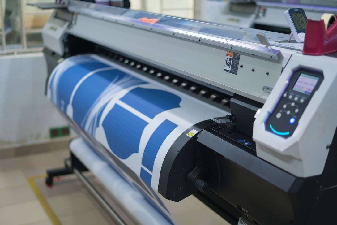 Impresora de gran formato imprimiendo una pancarta azul y blanca en un taller.