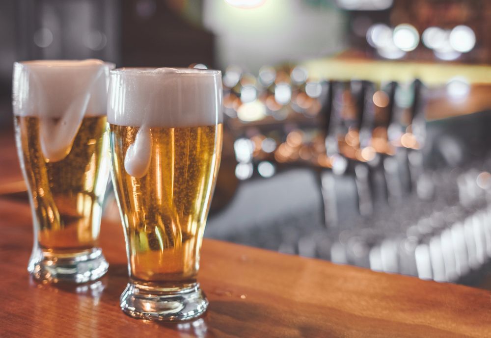 Two frosty pints of beer on a bar counter with a blurred pub background