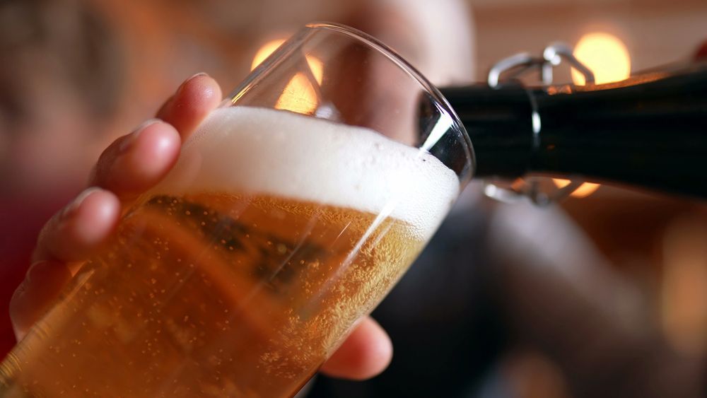 Hand pouring golden beer into a tilted glass, creating a foamy head