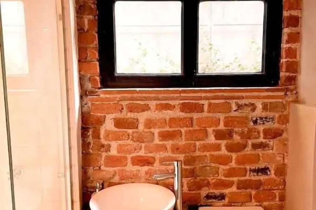 Un baño con pared de ladrillo, lavabo, inodoro y ventana.