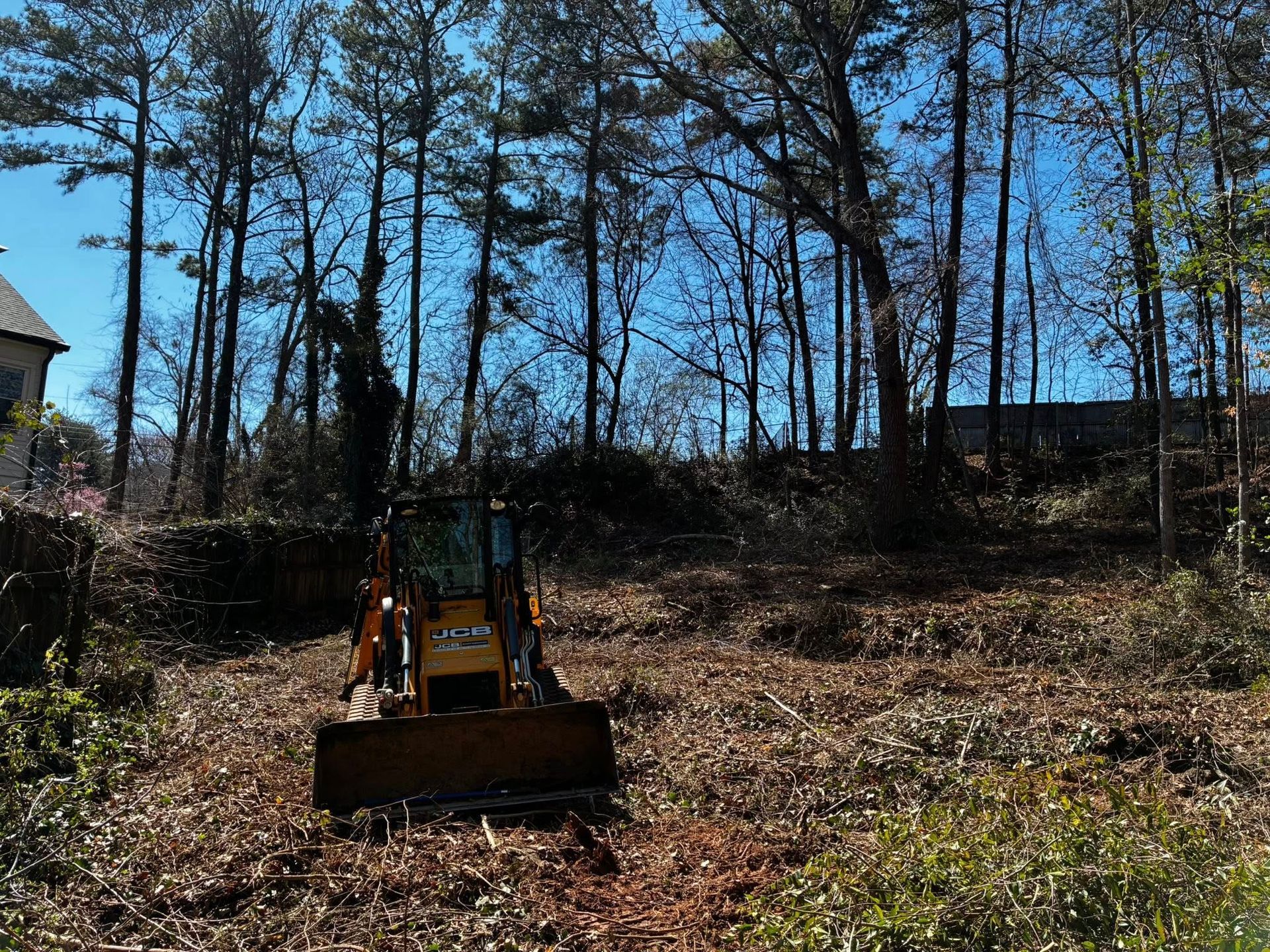 Yellow bulldozer clearing a wooded hillside under a bright blue sky