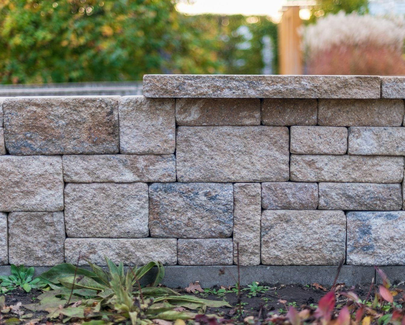 Stacked gray stone retaining wall with greenery and fallen leaves along the base