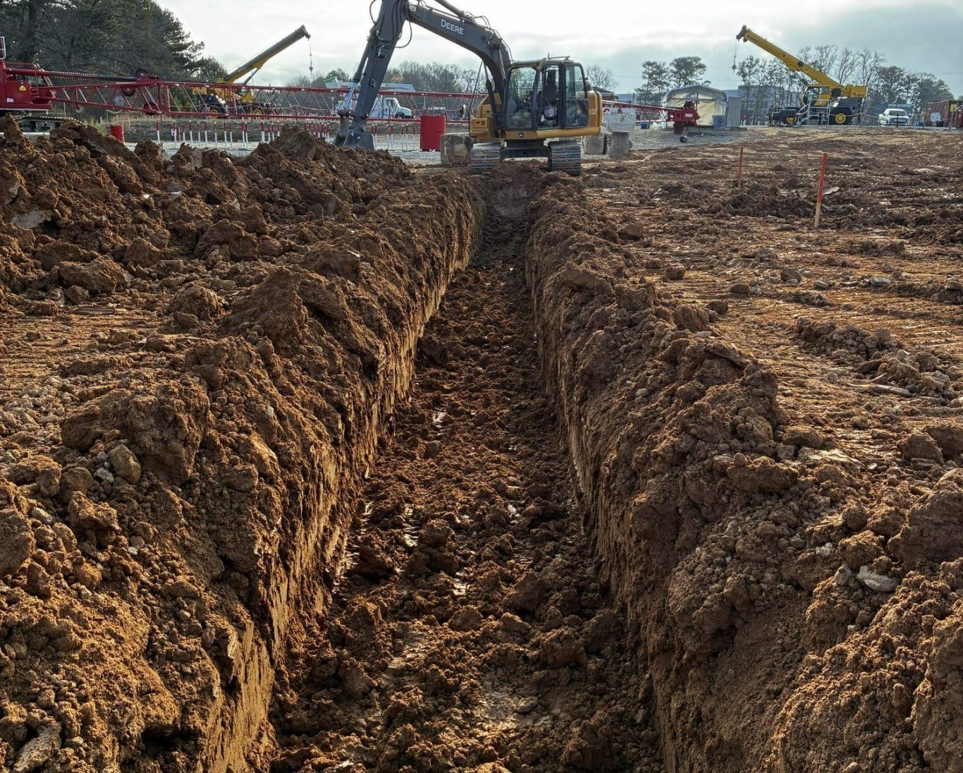 Excavators dig a long trench through muddy earth at a construction site.
