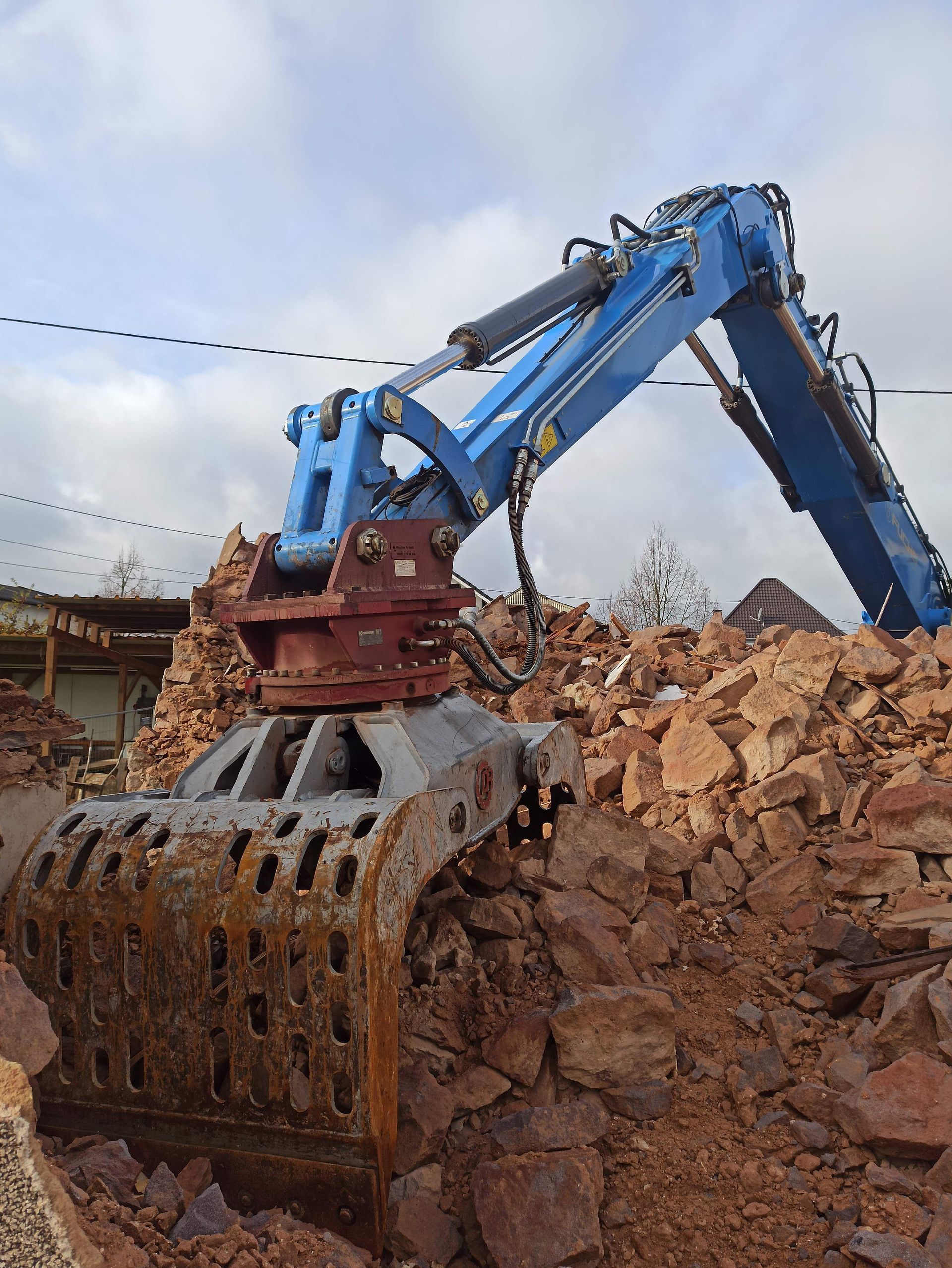 Blue excavator with a grapple bucket loading rubble at a demolition site