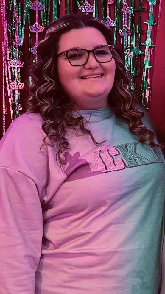 Autumn Harper in glasses and a pink shirt standing before a colorful tinsel backdrop