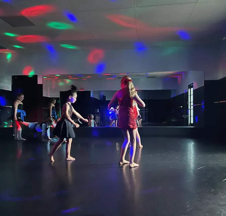A group of young dancers freestyle in a studio with colorful red, green, and blue lights on the ceiling