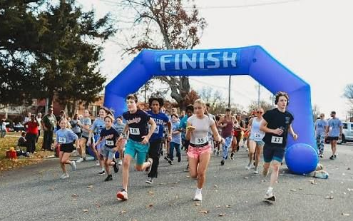 Runners sprint under a blue finish arch at Fit for Liberty event while spectators line the course.