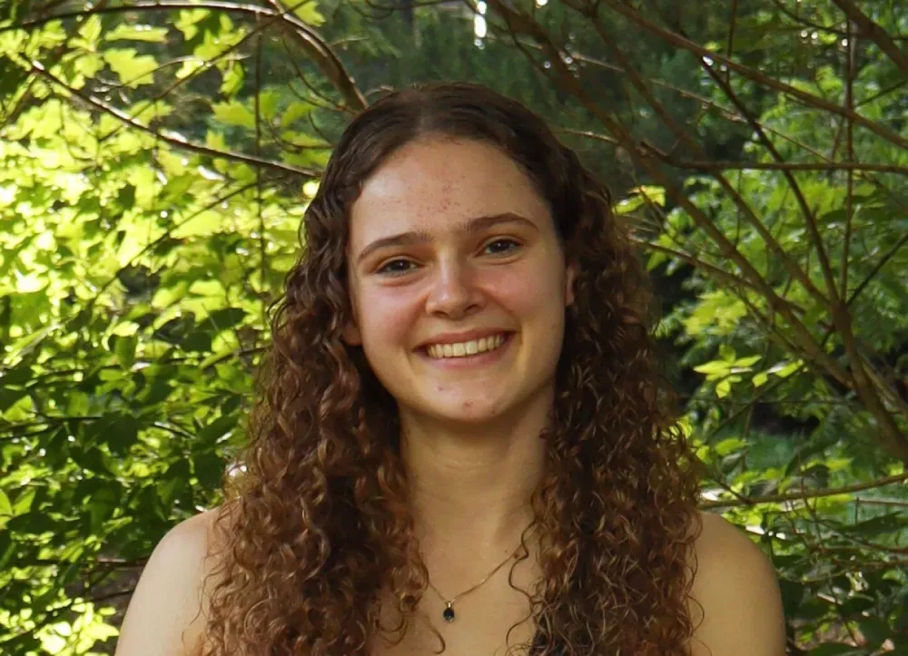 Portrait of Hayden Creech smiling outdoors in front of green foliage