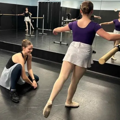Dance studio with mirrored wall; one dancer rehearses while the teacher provides instruction