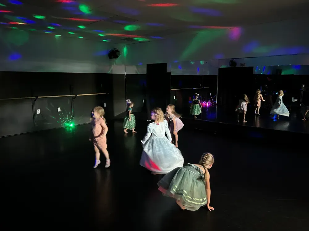 Children in pastel costumes dance in a mirrored studio with colorful disco lights.