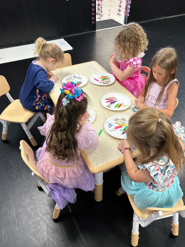 Children seated around a small table, painting paper plates in a classroom craft activity.