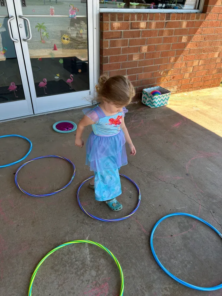 Child standing in colorful hula hoops on a concrete patio of the Southeast School of Dance