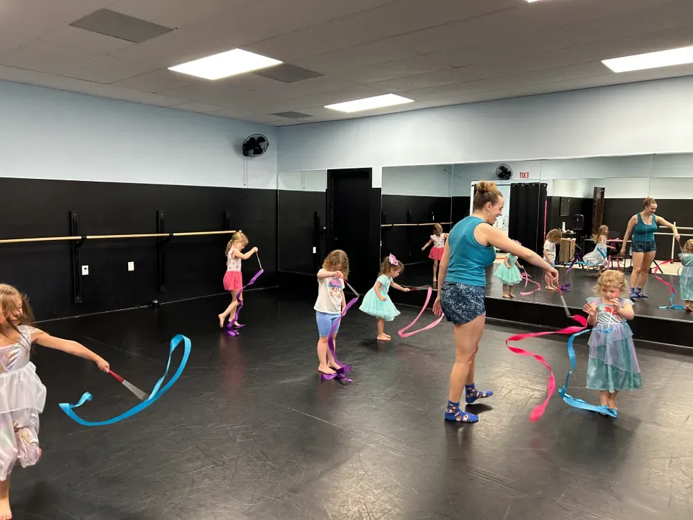 Children practicing ribbon dance in a studio with dance instructor Ms. Sidney