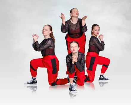 Four dancers in red pants and black tops posing in a studio against a white background