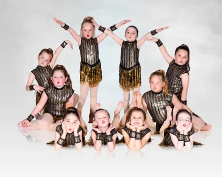 Young dancers in black and gold costumes posing in a choreographed formation on a white studio background